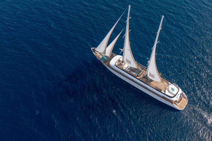Aerial view of a luxury gulet sailing yacht with white sails on deep blue Mediterranean waters.