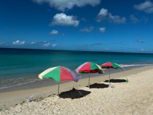 Three colorful beach umbrellas on sandy shore with turquoise ocean and blue sky with white clouds.